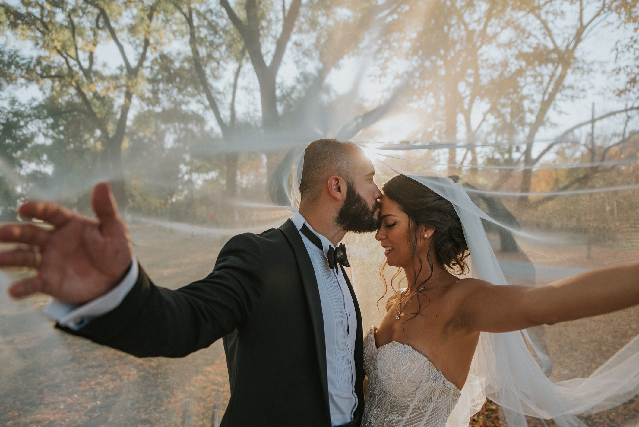 Bride and groom embracing under sunlight outdoors.