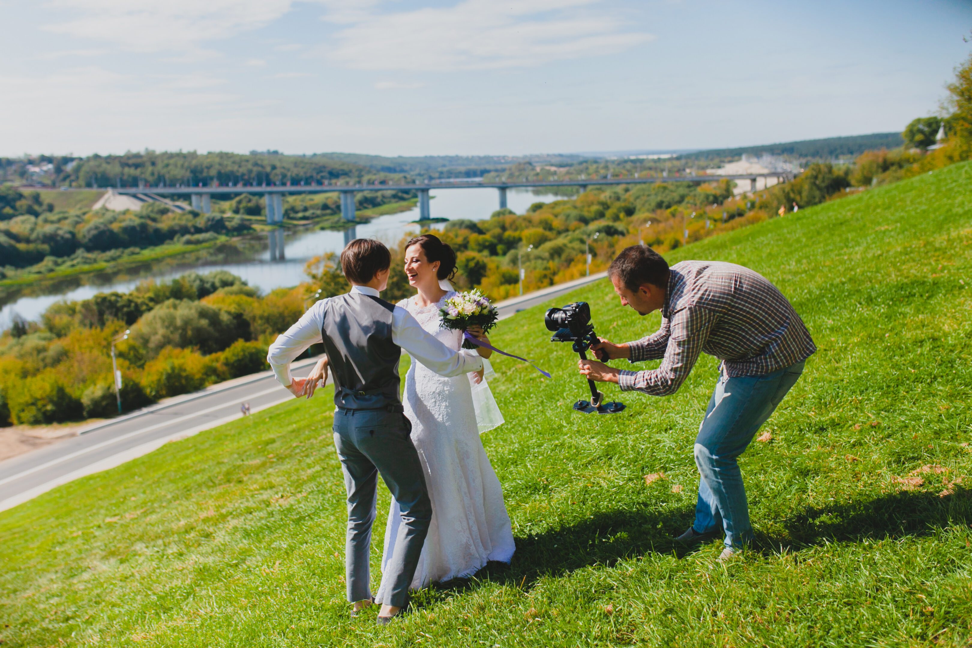 Wedding couple poses with videographer on hill.