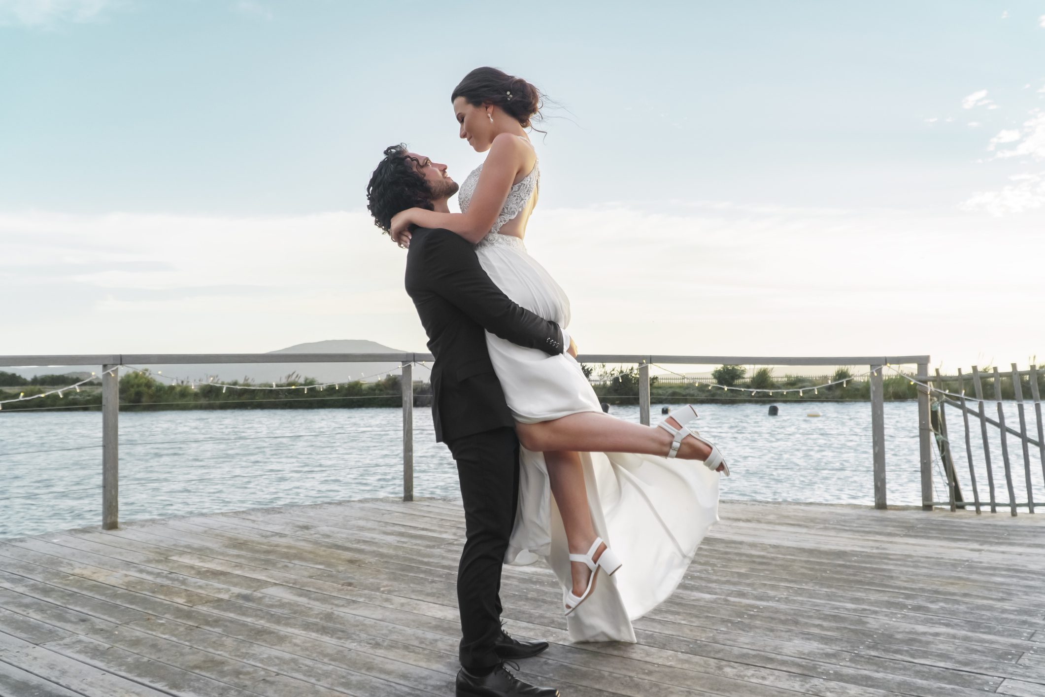 Bride and groom embrace by the water.